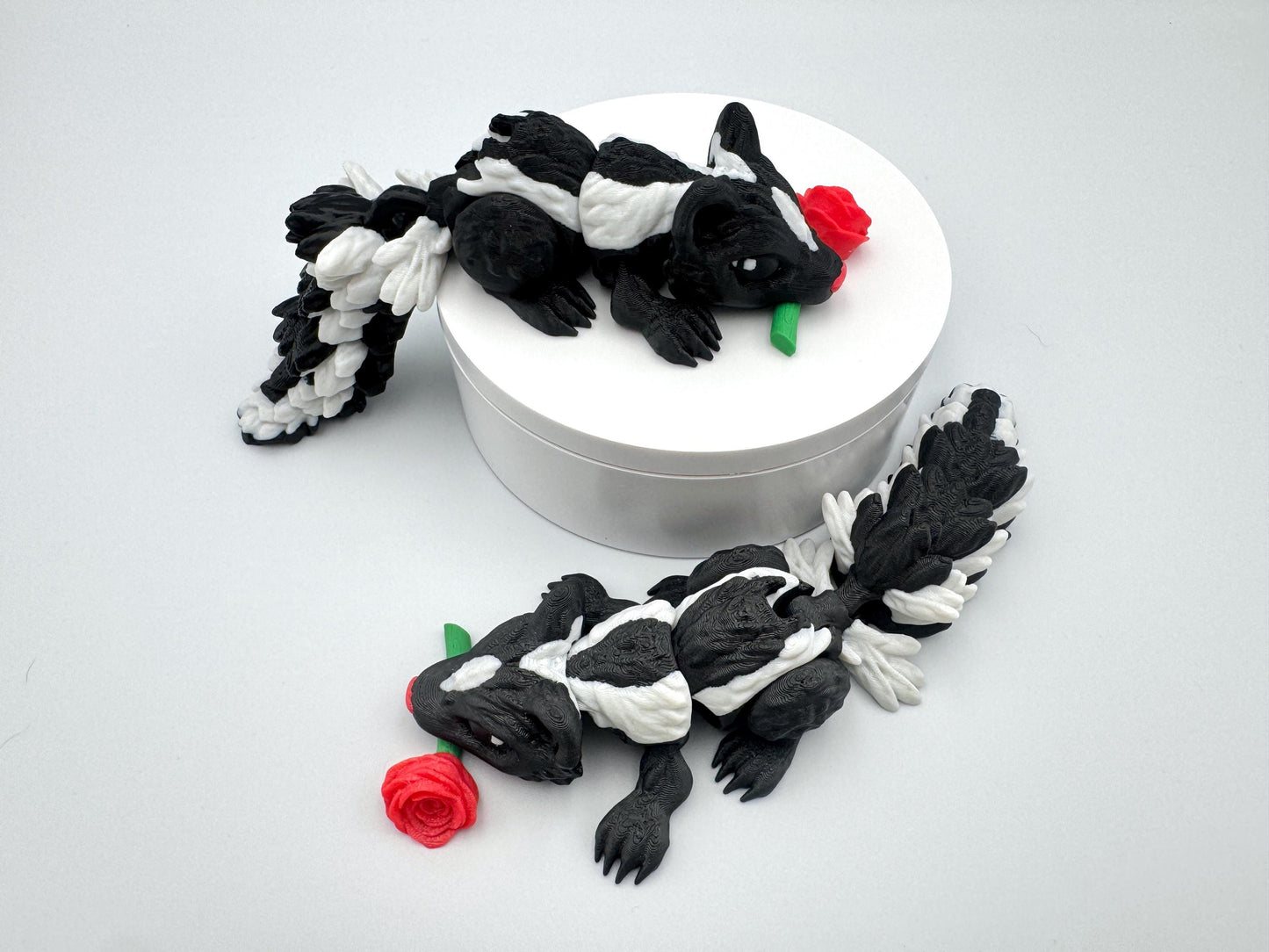 3D printed articulated Rose Skunk figurine featuring a black and white skunk holding a red rose in its mouth. The skunk has a flexible, segmented body and detailed texture, designed as a playful and charming Valentine’s Day decoration or collectible.