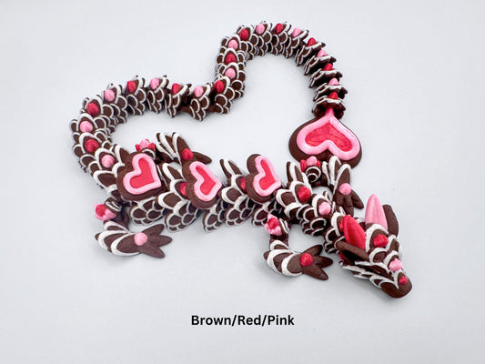 3D-printed articulated heart dragon cookie inspired fidget toy, with dark chocolate brown body, silk pink and silk red candy accents, white icing-like patterns and red hears with pink outline. Features intricate details and a fully flexible design.