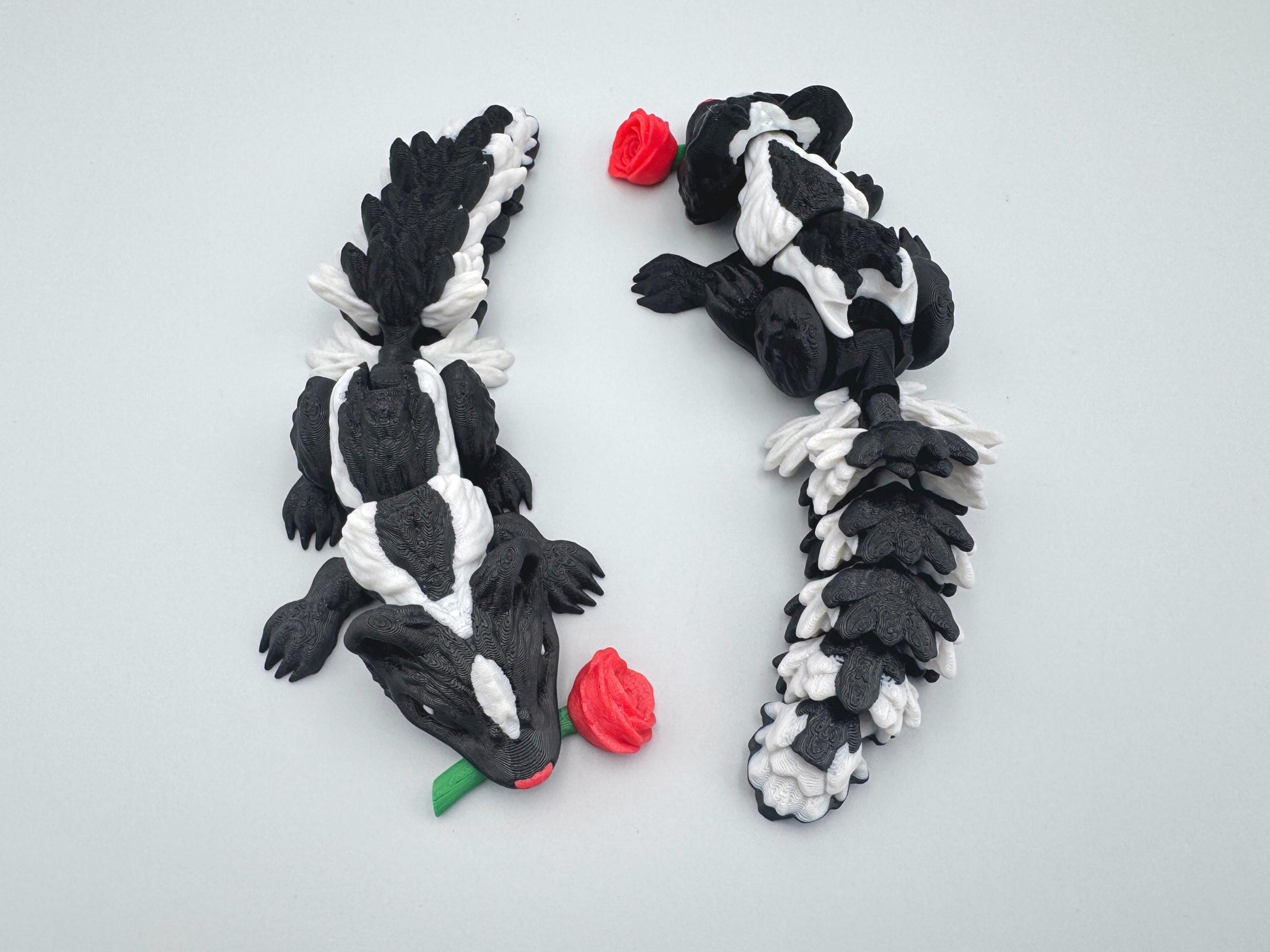 3D printed articulated Rose Skunk figurine featuring a black and white skunk holding a red rose in its mouth. The skunk has a flexible, segmented body and detailed texture, designed as a playful and charming Valentine’s Day decoration or collectible.