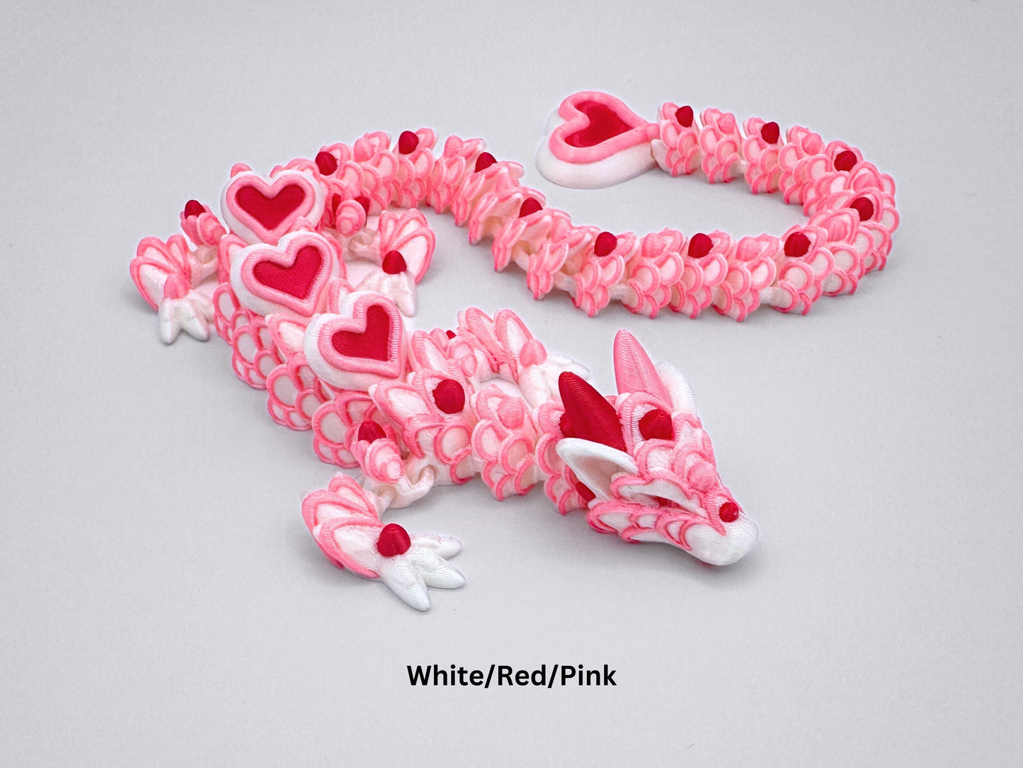 3D-printed articulated heart dragon, cookie inspired fidget toy with a white silk body, pink and red heart accents, and white frosting patterns. Features intricate details and a fully flexible design.