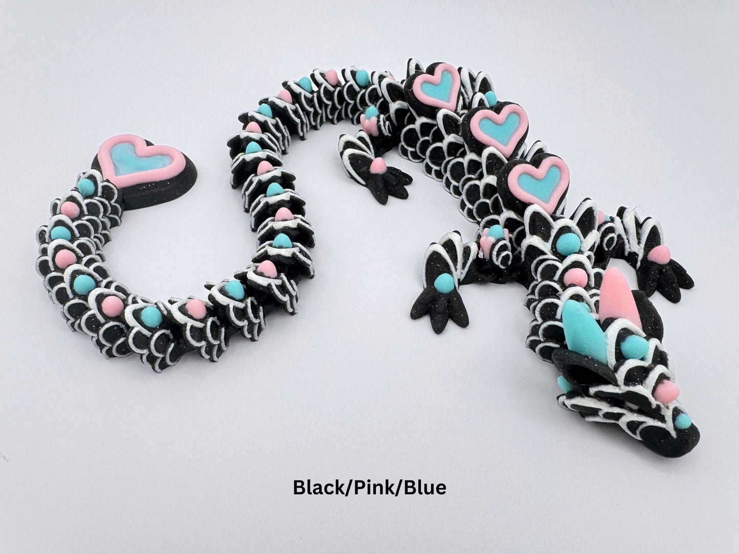 3D-printed articulated heart dragon cookie inspired fidget toy, with glitter black body, sakura pink and ice blue colors heart accents, and white frosting patterns. Features intricate details and a fully flexible design.