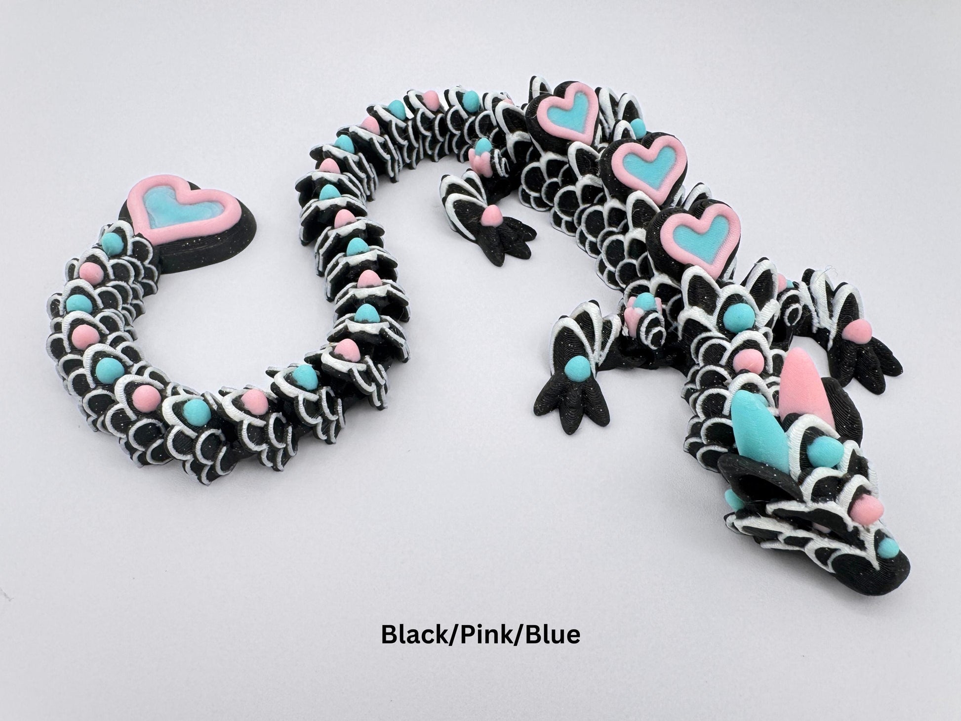 3D-printed articulated heart dragon cookie inspired fidget toy, with glitter black body, sakura pink and ice blue colors heart accents, and white frosting patterns. Features intricate details and a fully flexible design.