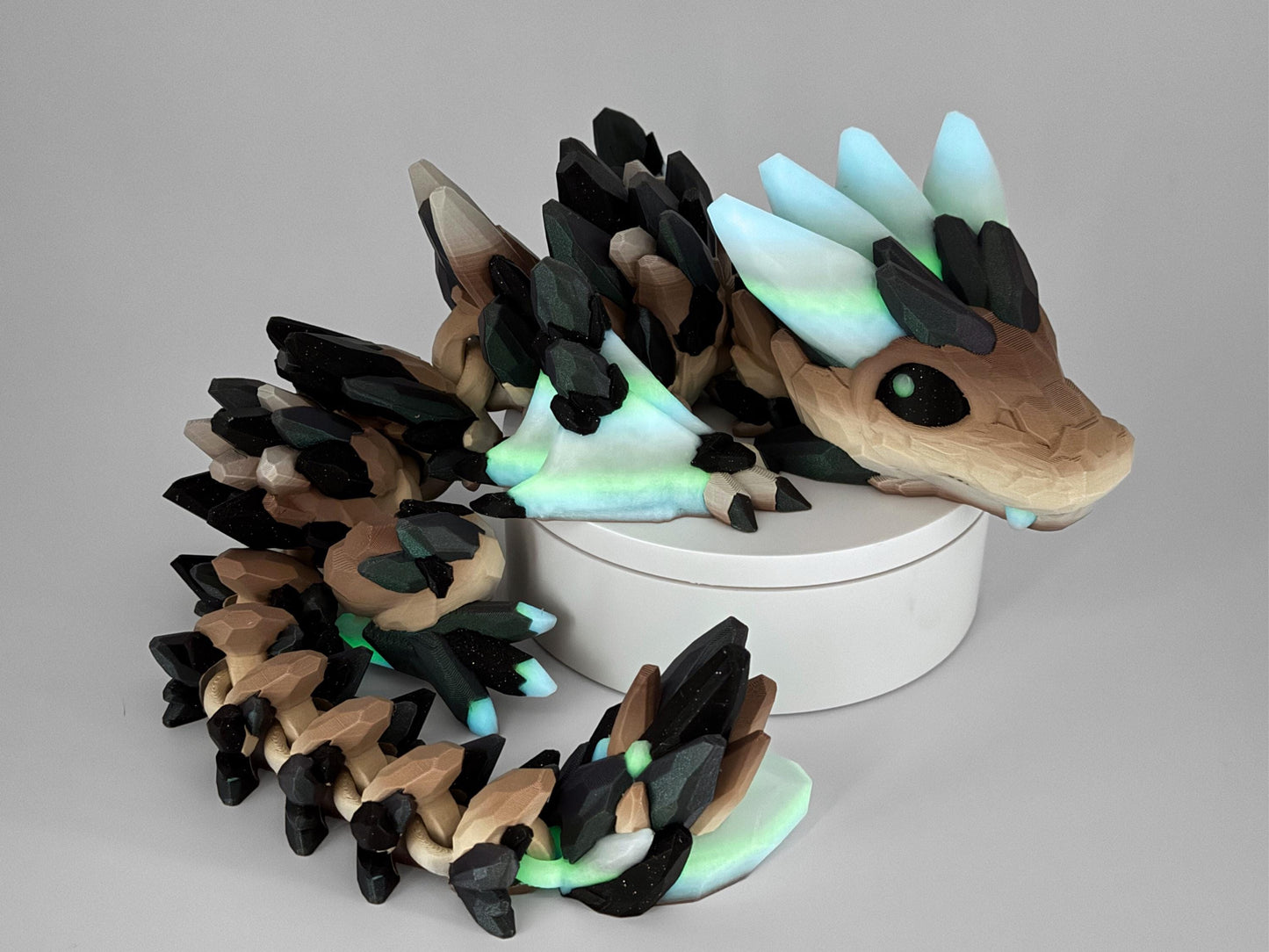 3D-printed Gemstone Baby Dragon fidget toy with an articulated body, featuring green, purple and black crystal scales and glow in the dark. The segmented design allows flexible movement, while the intricate faceted details mimic the look of precious gemstones, creating a striking and mystical aesthetic.
