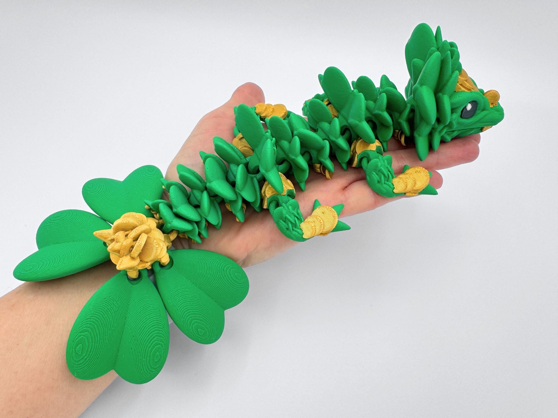 3D Printed Clover Dragon green gold and black articulated figurine with a clover 4 leaf design along its body. The dragon is made up of many small, overlapping leaves and has a large head with a wide mouth and large eyes. Used as desk decor for seasonal gift for St. Patrick’s Day.