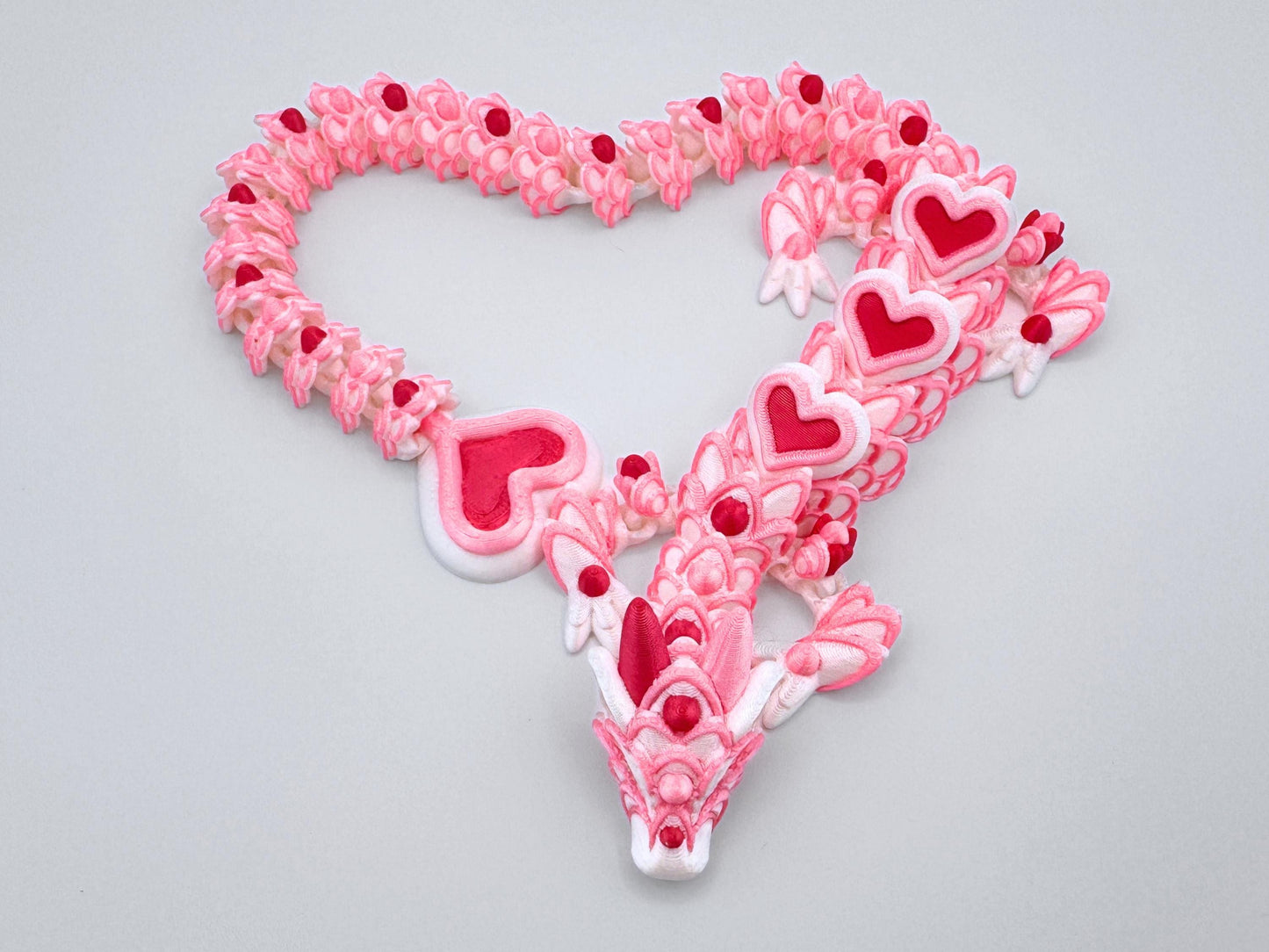 3D-printed articulated heart dragon, cookie inspired fidget toy with a white silk body, pink and red heart accents, and white frosting patterns. Features intricate details and a fully flexible design.