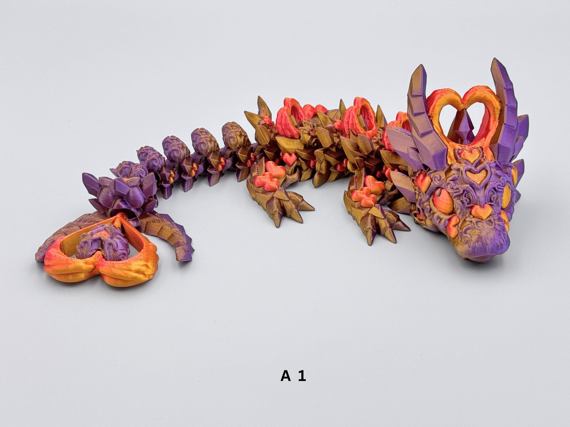 3D-printed Dark Heart Dragon fidget toy with an articulated body in purple and gold, adorned with intricate heart shaped details in red gold. Features heart-shaped horns and tail tip, segmented flexible design, and a fantasy-inspired aesthetic with rich metallic accents.