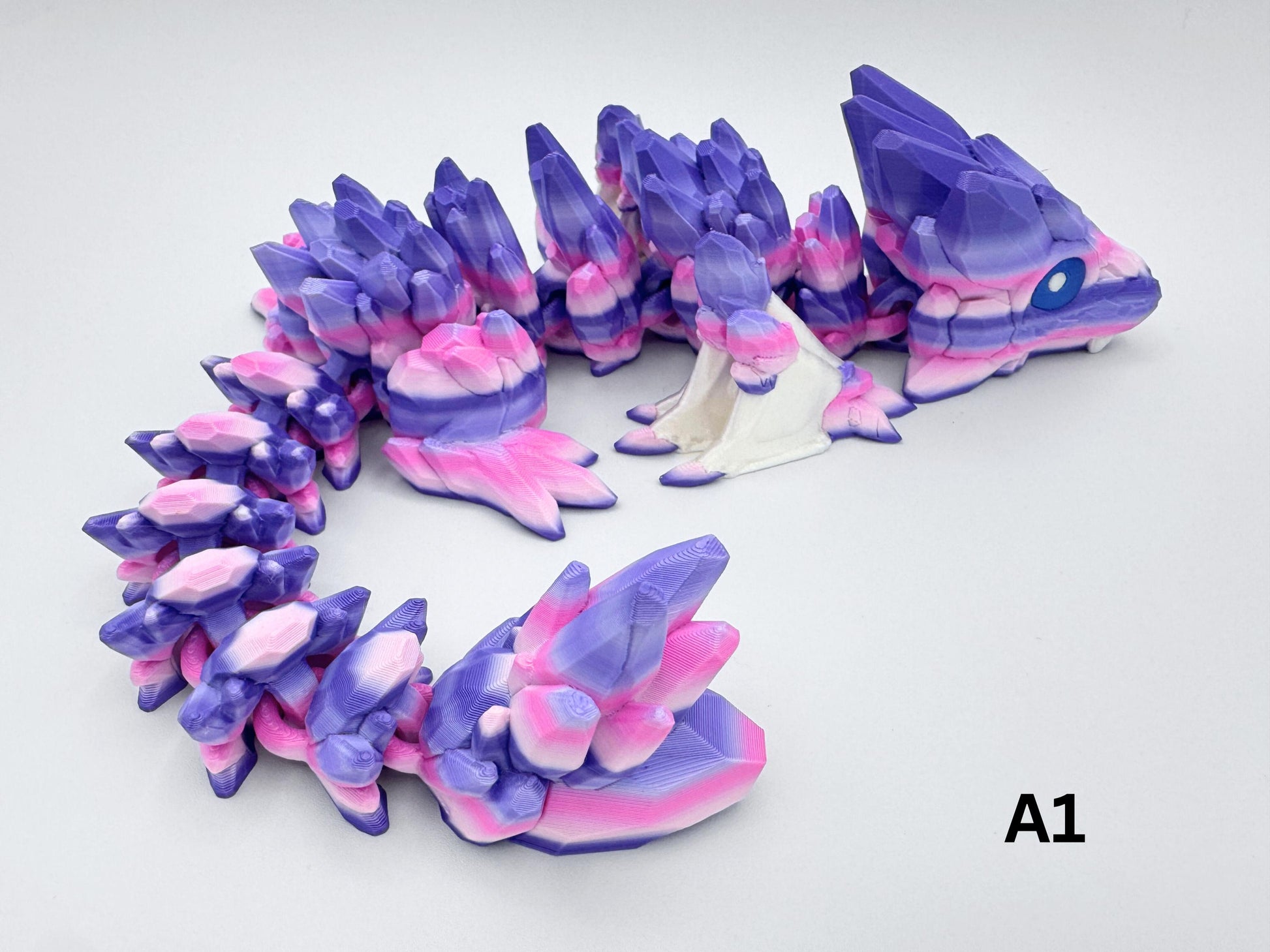 3D-printed Gemstone Baby Dragon fidget toy with an articulated body, featuring vibrant purple, pink, and white crystal-like scales. The segmented design allows flexible movement, while the intricate faceted details mimic the look of precious gemstones, creating a striking and mystical aesthetic.