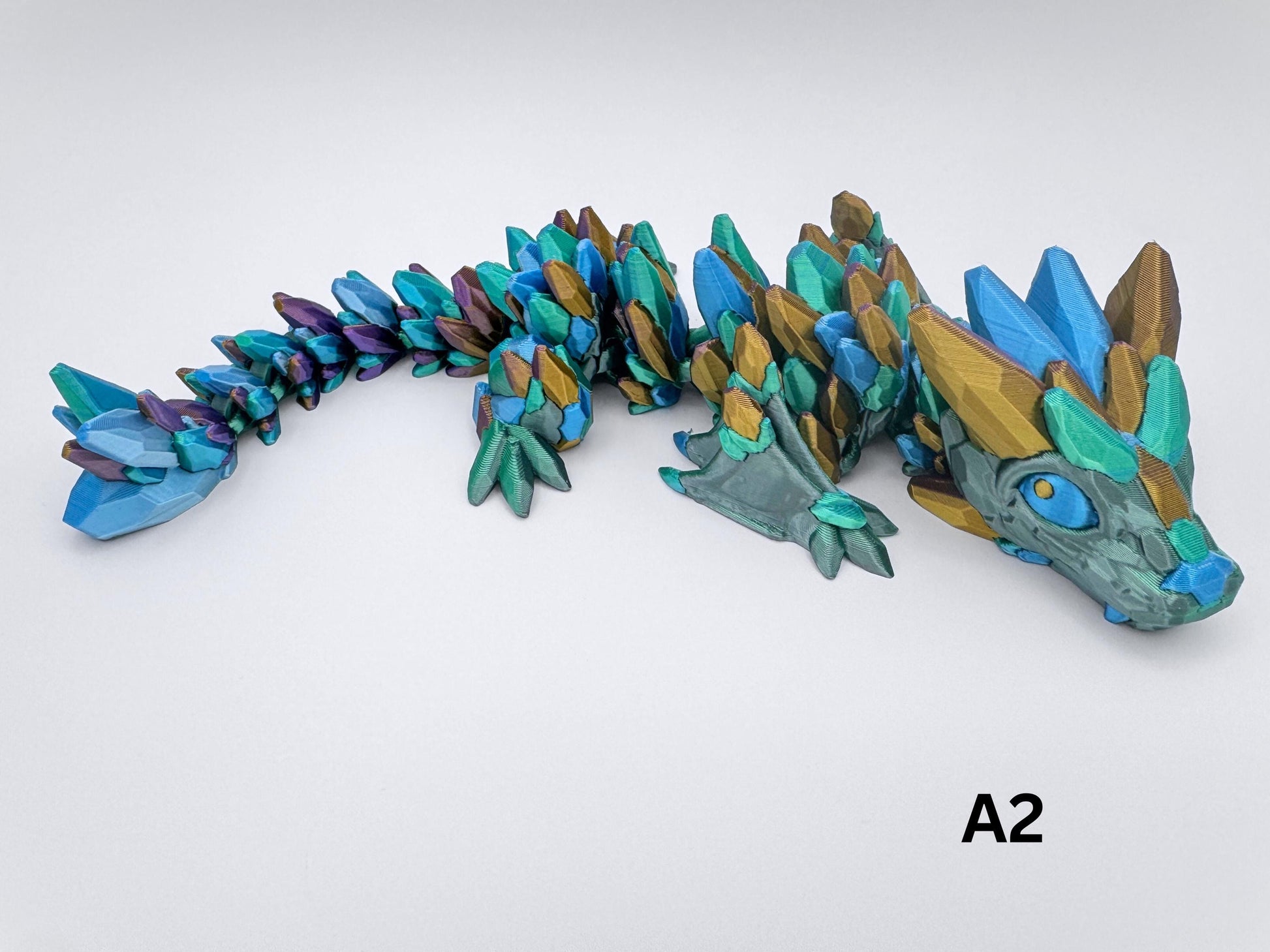 3D-printed Gemstone Baby Dragon fidget toy with an articulated body, featuring green, purple, gold and blue silver crystal scales. The segmented design allows flexible movement, while the intricate faceted details mimic the look of precious gemstones, creating a striking and mystical aesthetic.