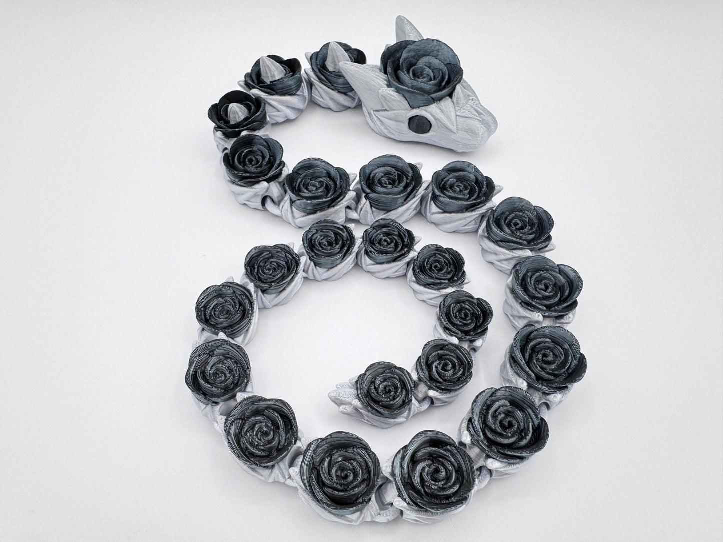 Silver and black articulated snake figurine posed in an S-curve. Each rose-shaped segment transitions smoothly, mimicking real movement. The headpiece includes a central black rose with subtle horn details, emphasizing the dark floral fantasy theme across the full body.