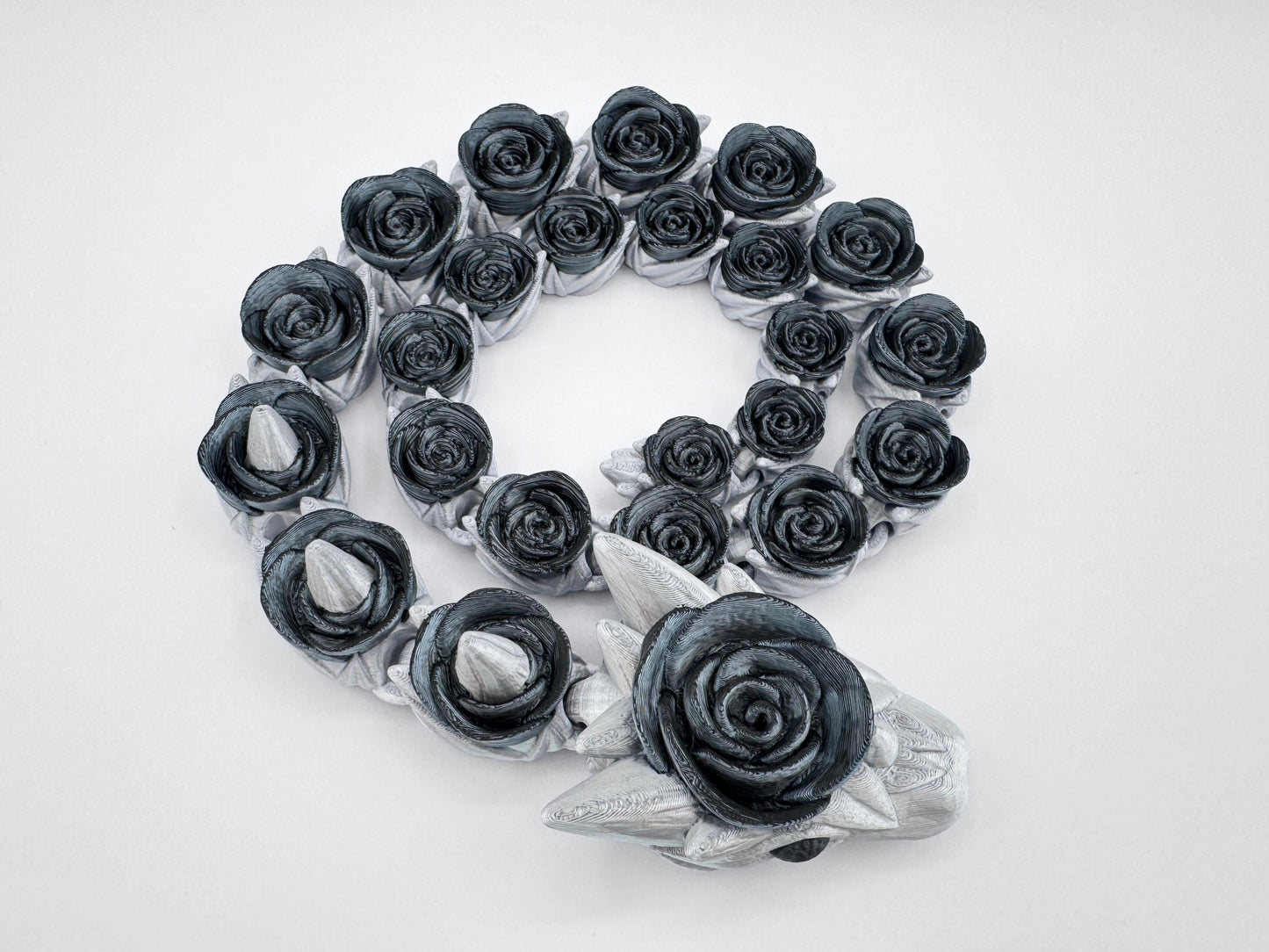 Gothic black rose snake fully coiled with visible sculpted horns on the head. Silver and black filament contrasts along the articulated spine, highlighting the elegance of the linked rose pattern. The image captures symmetry and detail across the entire 3D printed figurine.