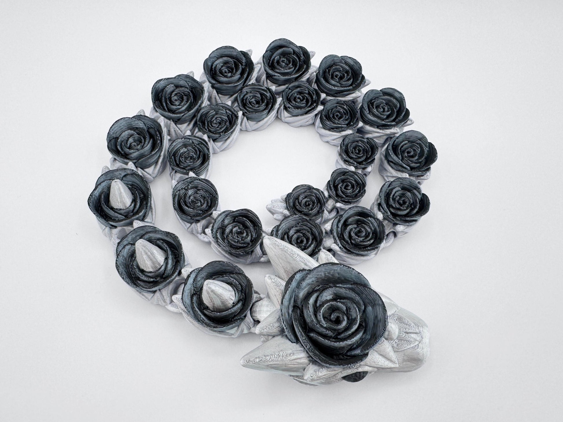 Gothic black rose snake fully coiled with visible sculpted horns on the head. Silver and black filament contrasts along the articulated spine, highlighting the elegance of the linked rose pattern. The image captures symmetry and detail across the entire 3D printed figurine.