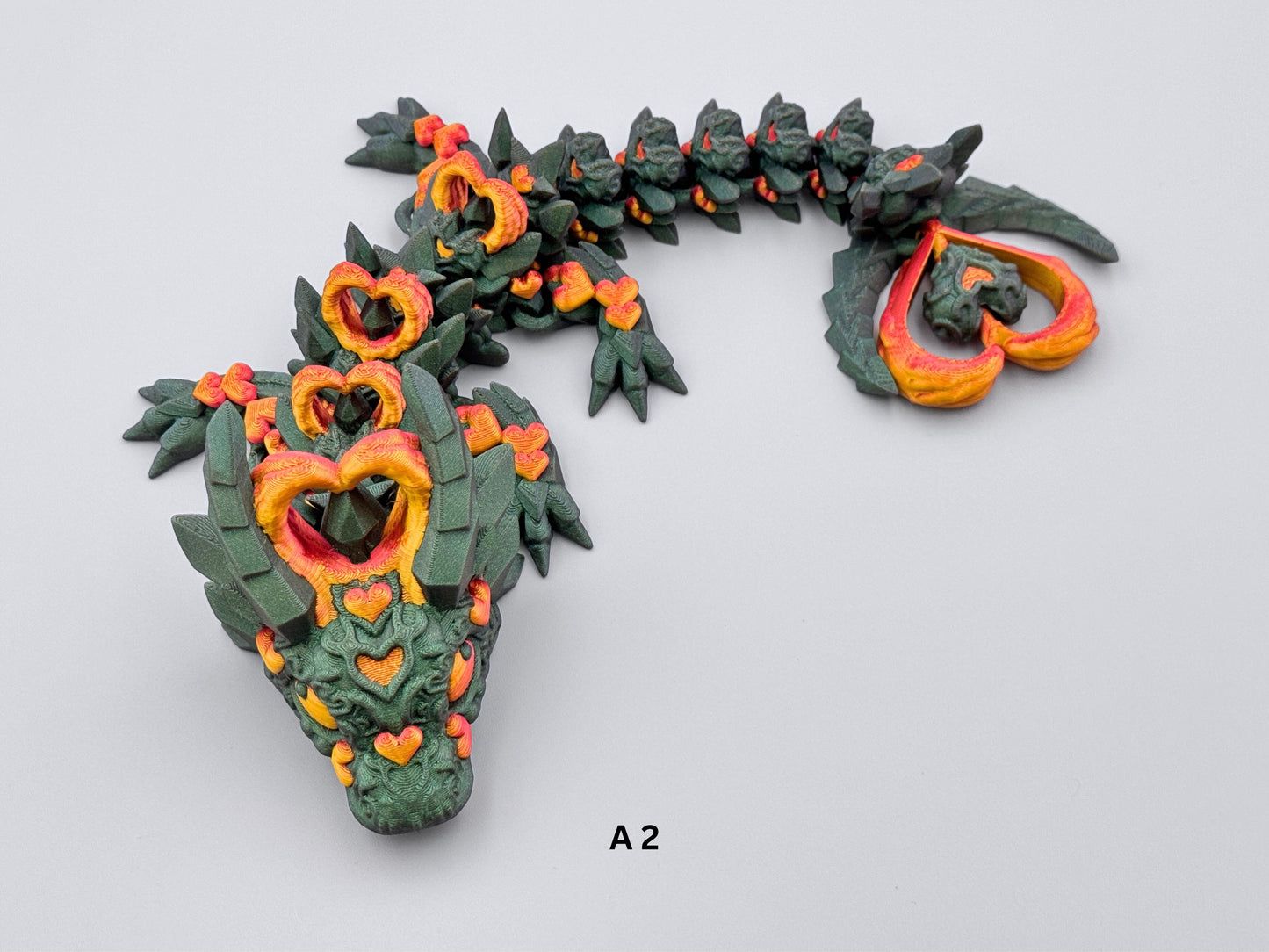 3D-printed Dark Heart Dragon fidget toy with an articulated body shifting from green to purple, adorned with intricate red-gold heart details. Features heart-shaped horns and tail tip, a segmented flexible design, and a fantasy-inspired aesthetic with rich metallic accents.