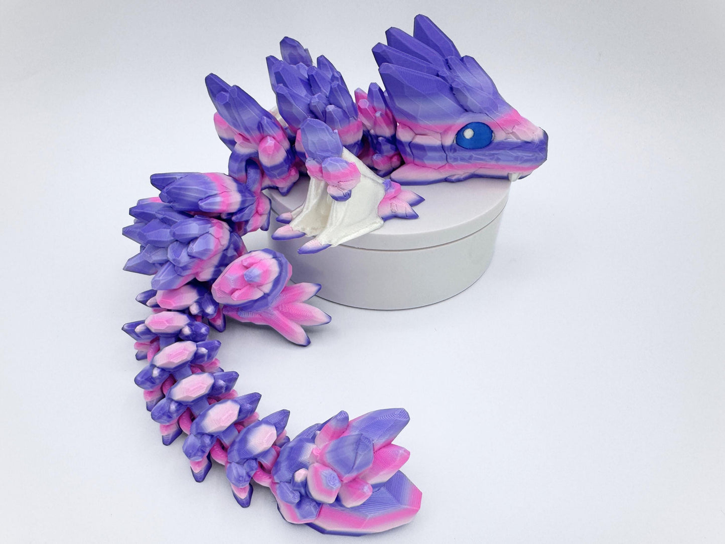 3D-printed Gemstone Baby Dragon fidget toy with an articulated body, featuring vibrant purple, pink, and white crystal-like scales. The segmented design allows flexible movement, while the intricate faceted details mimic the look of precious gemstones, creating a striking and mystical aesthetic.