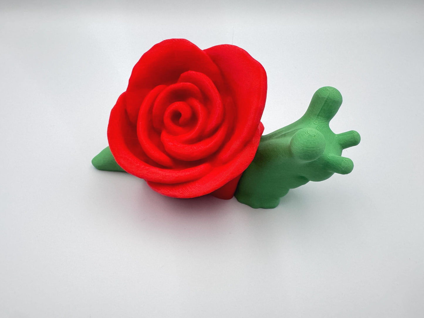 3D-printed articulated rose snail figurine with a vibrant red rose on its back and a bright green body. This cute and whimsical fidget toy is a perfect collectible, desk companion, or unique gift for nature and snail lovers.