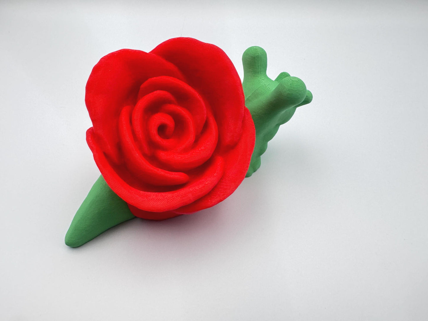 3D-printed articulated rose snail figurine with a vibrant red rose on its back and a bright green body. This cute and whimsical fidget toy is a perfect collectible, desk companion, or unique gift for nature and snail lovers.