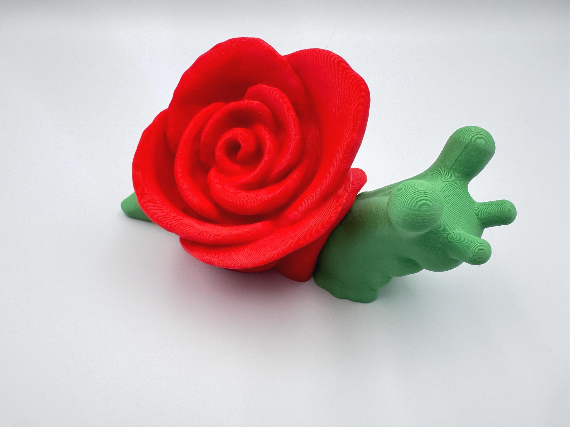 3D-printed articulated rose snail figurine with a vibrant red rose on its back and a bright green body. This cute and whimsical fidget toy is a perfect collectible, desk companion, or unique gift for nature and snail lovers.