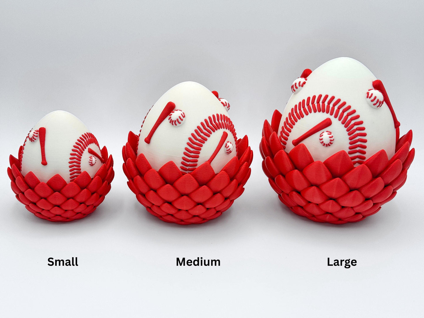 Three sizes of 3D printed Baseball Dragon eggs labeled Small, Medium and Large, each with red baseball stitching and red dragon scale bases, aligned side by side for comparison.