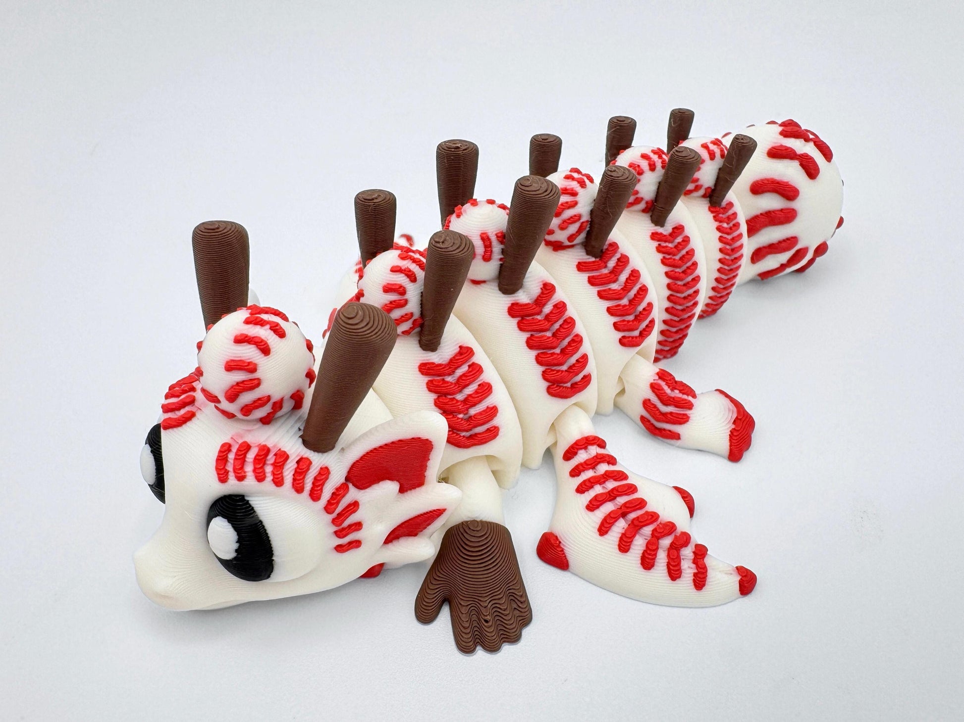 Close-up of a 3D printed Baseball Dragon figurine with red stitching details, white body, brown bat-shaped spines, and expressive black-and-white eyes, capturing its textured articulation.