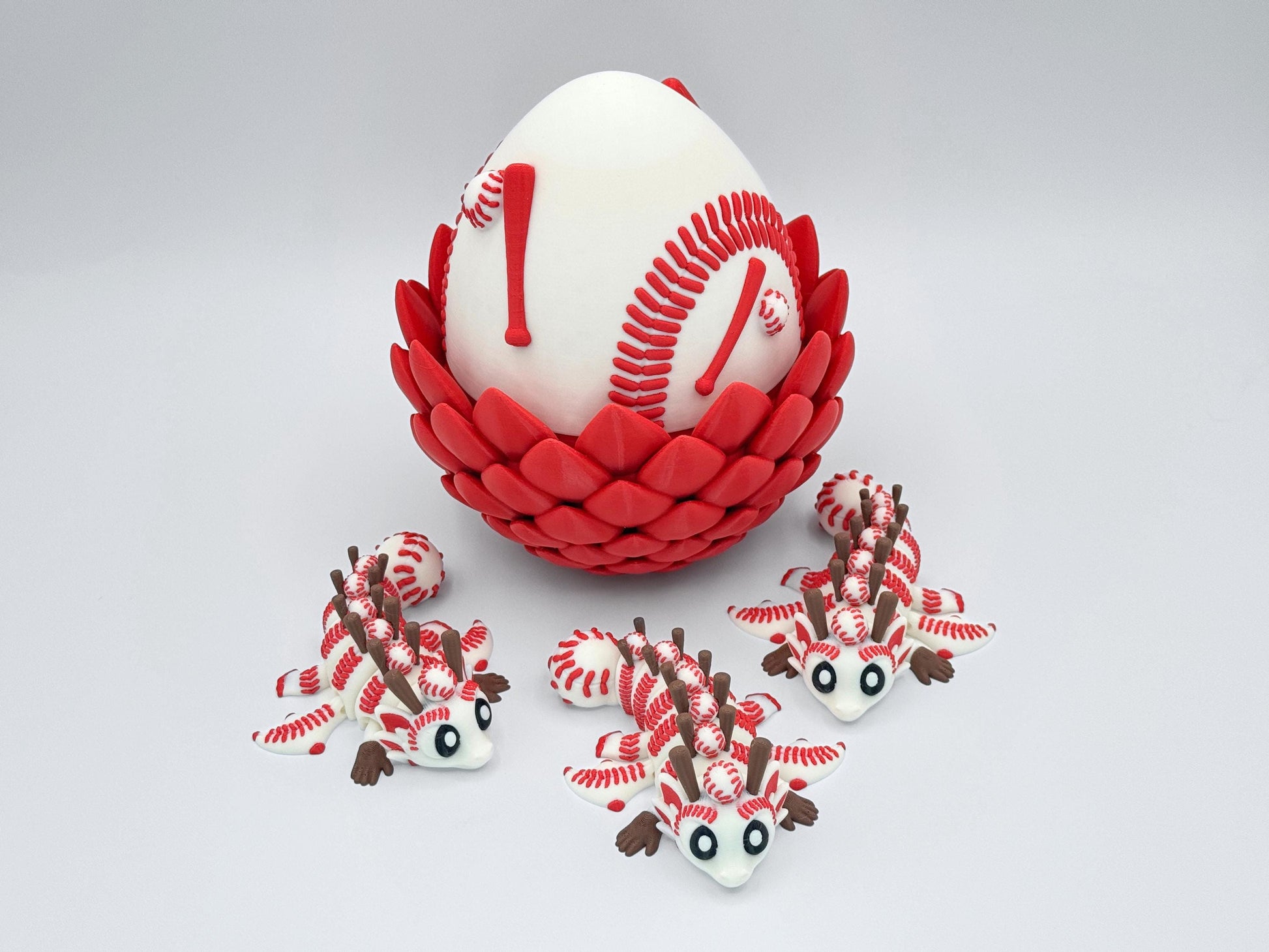 3D printed Baseball Dragon set featuring a large white egg with red baseball stitching details, seated in a red petal style base, surrounded by three articulated dragon figurines with baseball textured heads, red stitching, brown horns and white bodies.