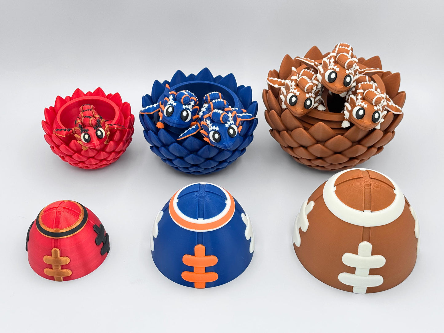 Three football dragon eggs opened to reveal matching articulated dragons inside. Red and gold dragon in small egg, blue and orange dragons in medium egg, and brown and white dragons in large egg. Egg tops are removed and placed in front.