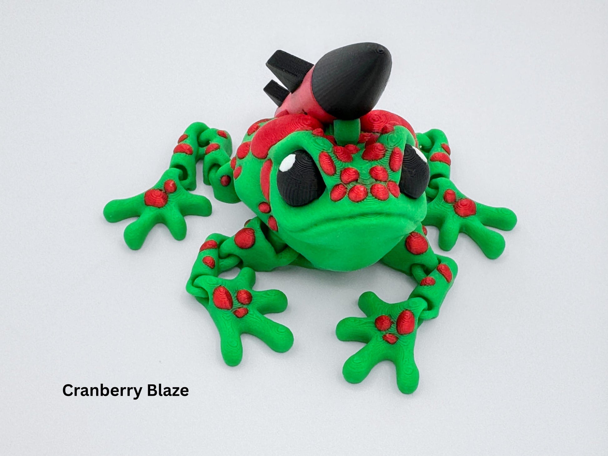 Frontal perspective of the green and red Missile Toad figurine with a large rocket mounted along the back. Frog sits crouched with wide feet and raised red spots. The print layers and vibrant colors show clearly from this angle.