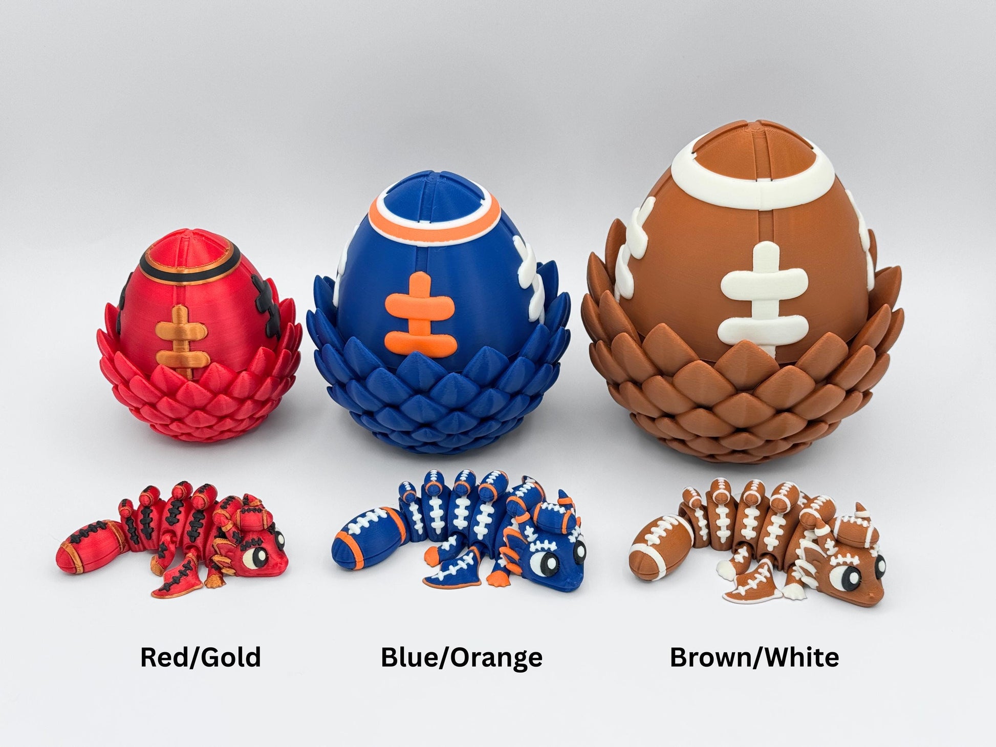 Closed red and gold, blue and orange, and brown and white football dragon eggs with matching articulated dragons posed in front. Dragons have flexible segmented bodies, football lace accents, and 3D printed football-shaped tails.