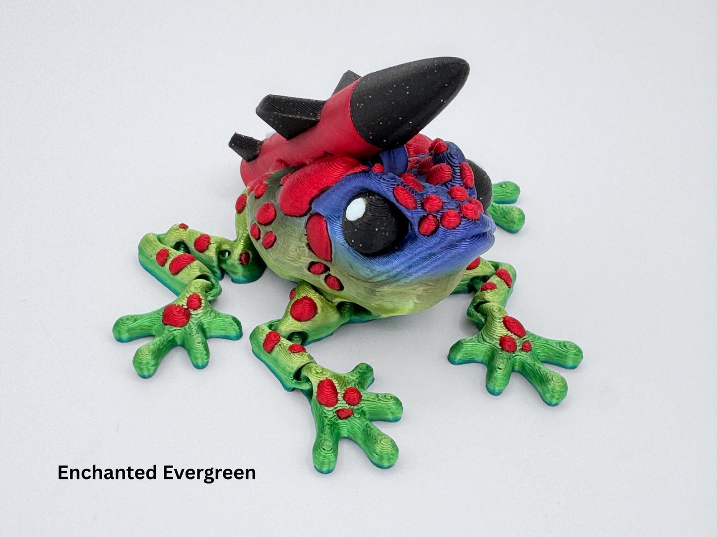 Close-up view of the 3D printed Missile Toad with a blue face, green limbs and raised red spots. A red and black rocket with white “USA” lettering is attached to its back. The textured filament details and bold color contrast give this frog a playful, high-impact holiday look.