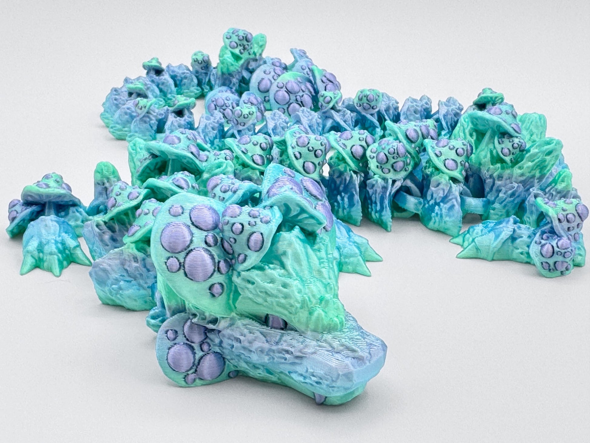 Close-up frontal shot of the dragon’s head and upper body. The pastel green snout is detailed with raised lavender mushrooms, while the articulated spine behind it fades from mint to pale blue. Textured mushrooms continue down its back and tail.