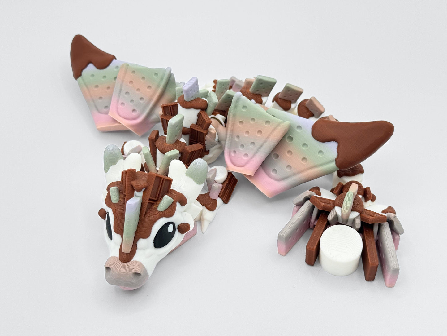 Front-facing S’mores Dragon with chocolate horns, graham cracker wings, and marshmallow tail. A 3D printed fantasy figurine with articulated motion and dessert themed features.