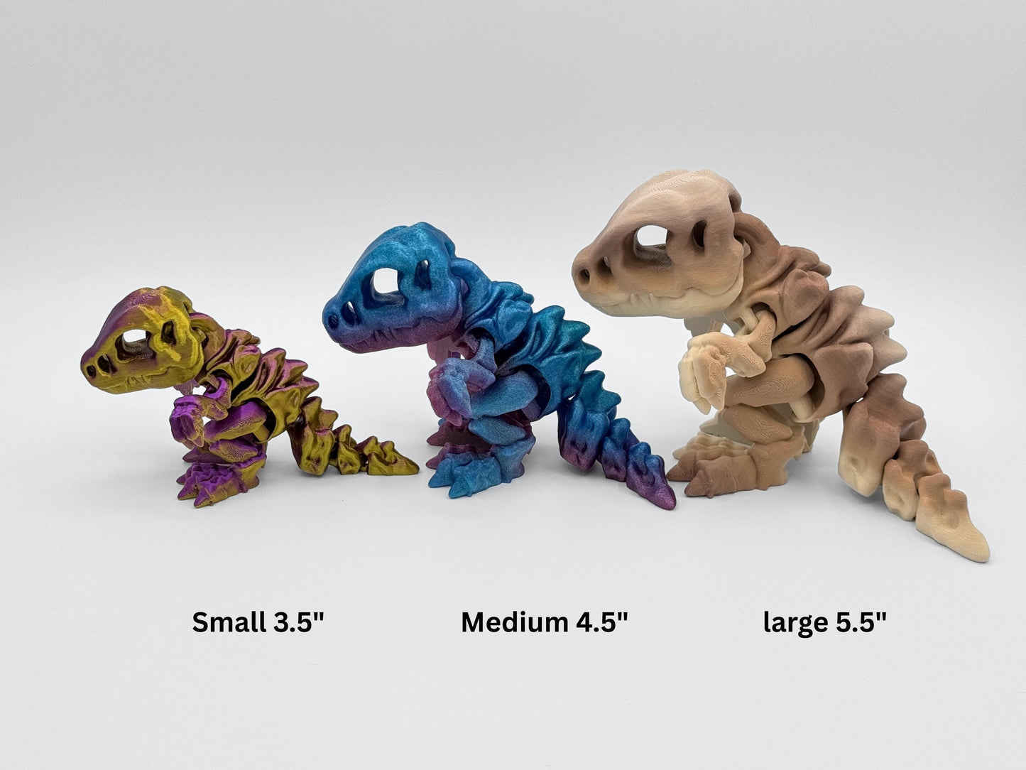 Three articulated 3D printed dinosaurs in a size comparison, shown in gold-purple, rainbow gradient and tan brown colors. The figurines are labeled small 3.5", medium 4.5", and large 5.5" to show scale differences.