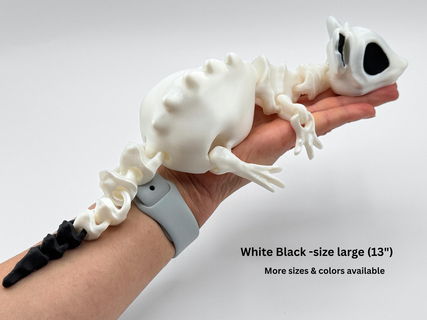 Articulated bone rat skeleton figurine in white with black eye sockets and tail tip, shown resting across a hand for size reference. The body length measures approximately 13 inches.