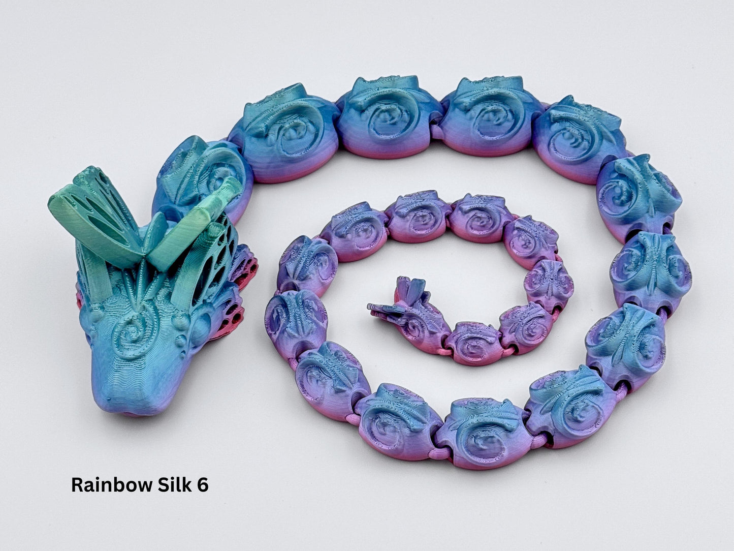 3D printed articulated butterfly snake with rose-shaped body segments, silky gradient blue teal to purple pink colors, posed in a circle on a clean white background.