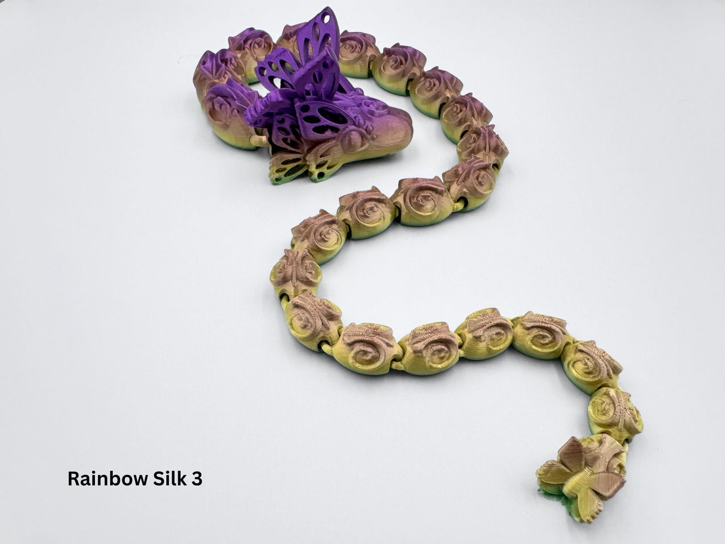3d Printed Butterfly Snake features a sleek, elongated body with smooth, sinuous curves, sharp ridges along its spine, and a striking blend of vibrant bronze and purple scales that enhance its serpentine elegance.