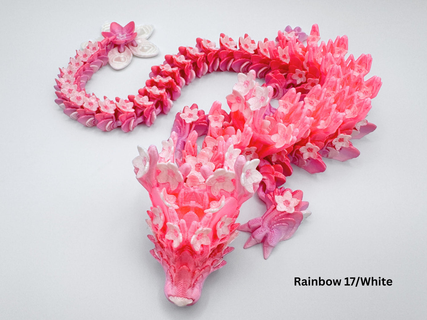 3D printed articulated Cherry Blossom dragon in gradient pink and peach. The dragon figurine features blossom-shaped scales and a flower tail, curled into a wide display pose.