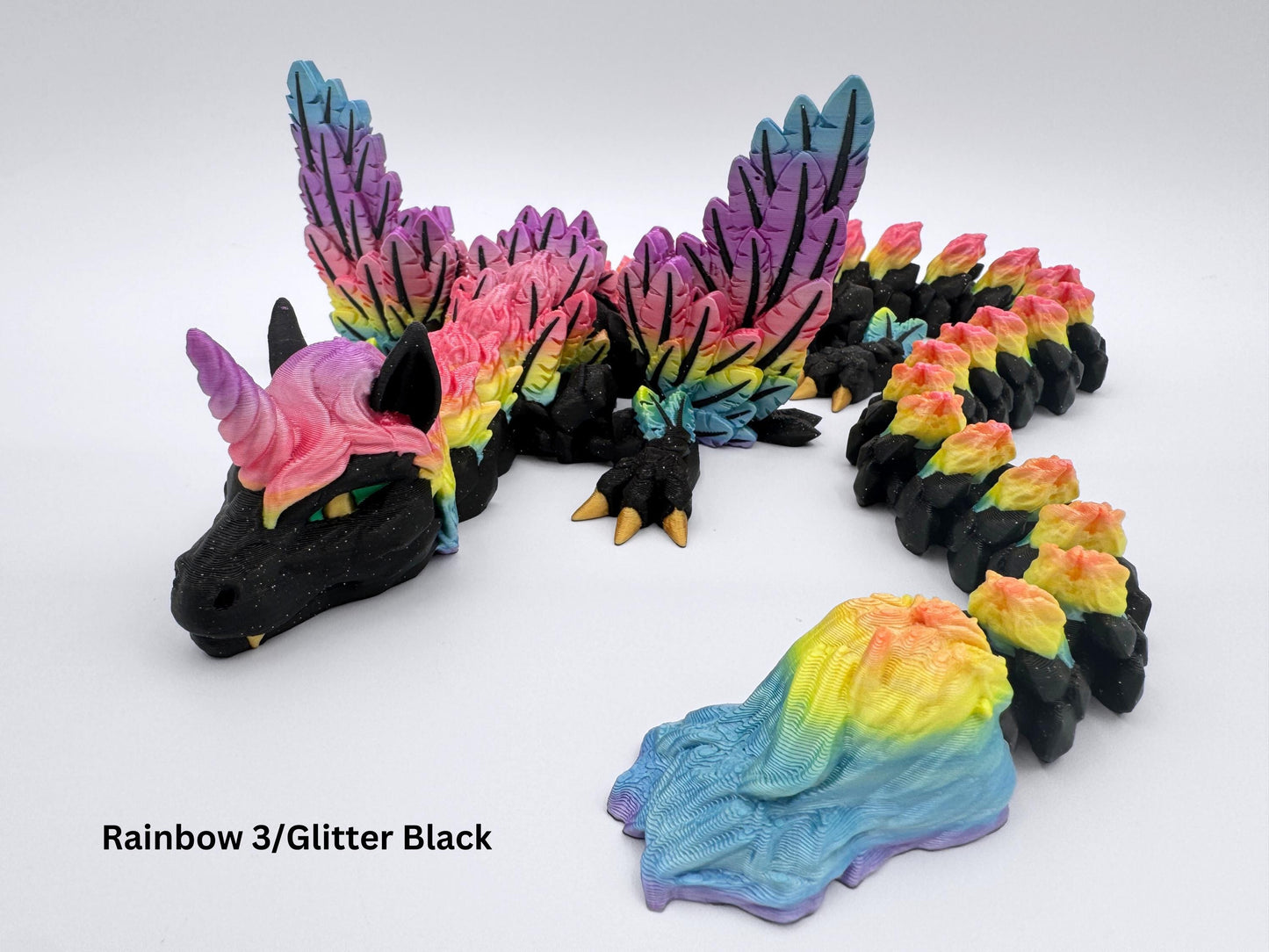 3D Printed Unicorn Dragon Fidget in glitter black with rainbow gradient wings, mane, and tail. The articulated figurine is stretched forward, showing detailed feathered wings, curved horn, and segmented body.