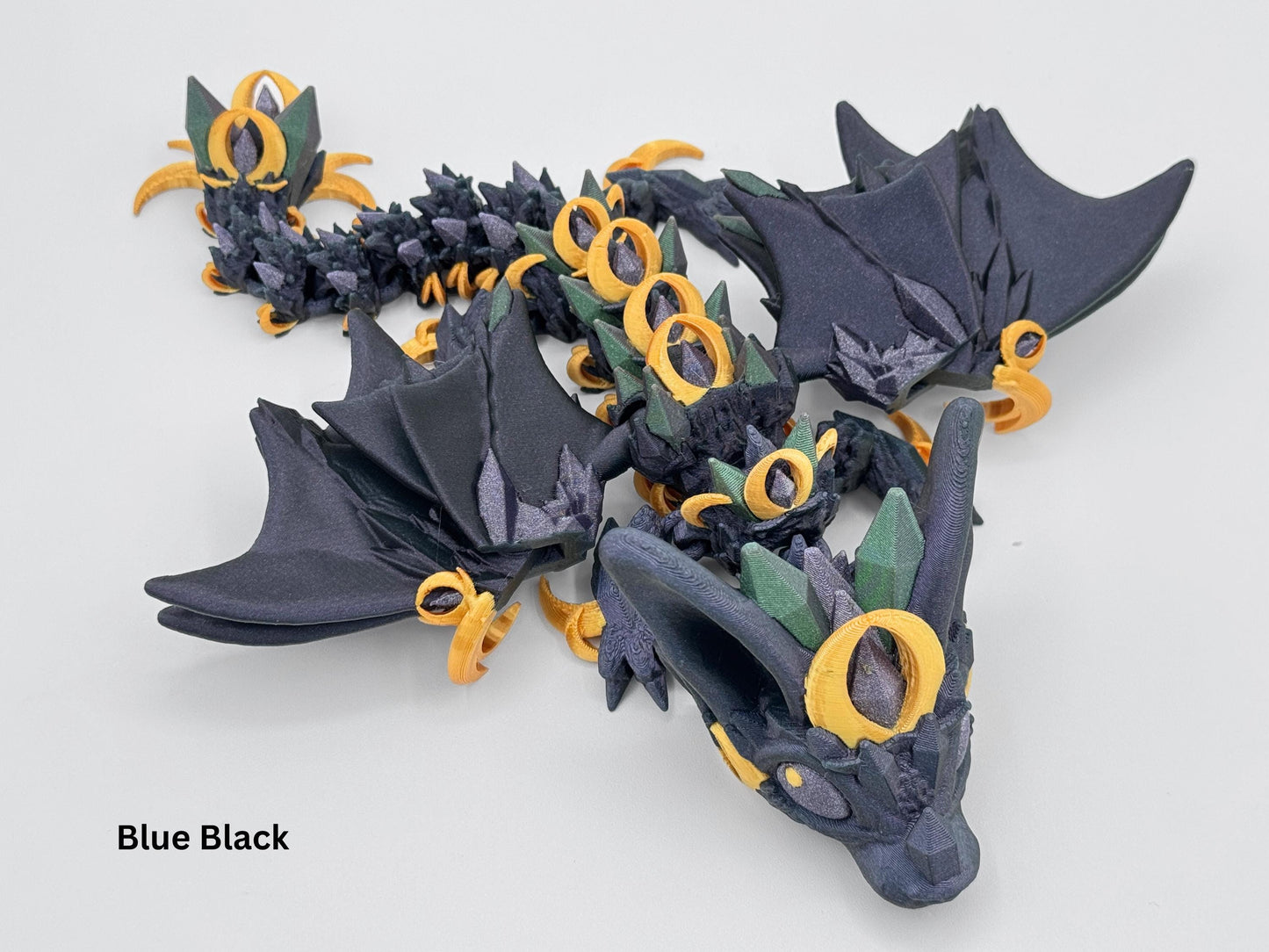 Night wing dragon figurine in simmer black and midnight blue with gold and purple green accents. The flexible dragon body is adorned with crystal style details. 3D printed figurine for fantasy decor or fidgeting, posed flat in a serpentine shape.