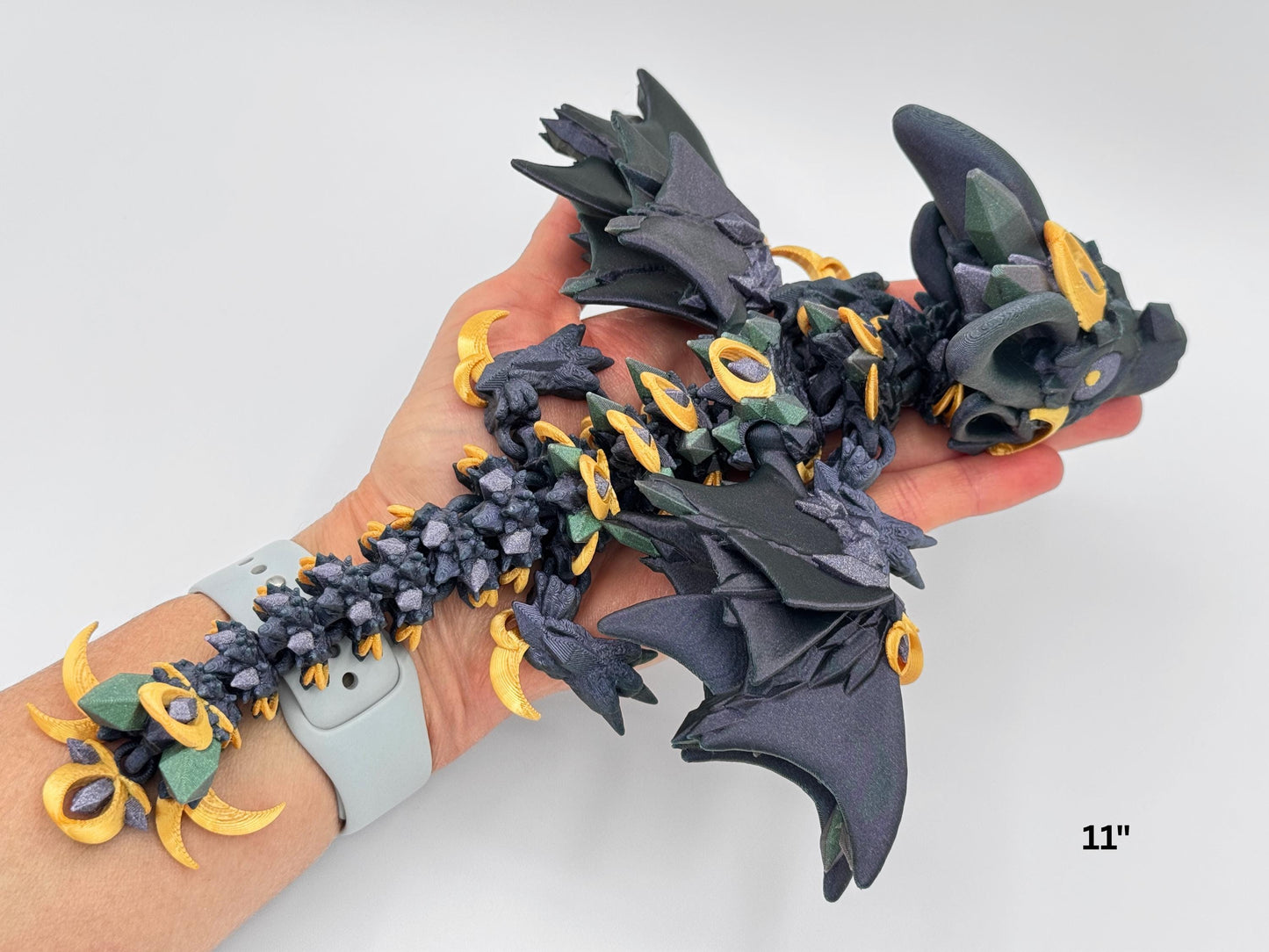 Night Wing Dragon held in hand to show scale and flexibility in shimmering black and blue tones. Articulated body curves gently in a resting pose, with crystal-textured back, ear-shaped side details, and wings partially folded. Highlights the dragon’s compact size and hand-fit design for fidgeting or display.
