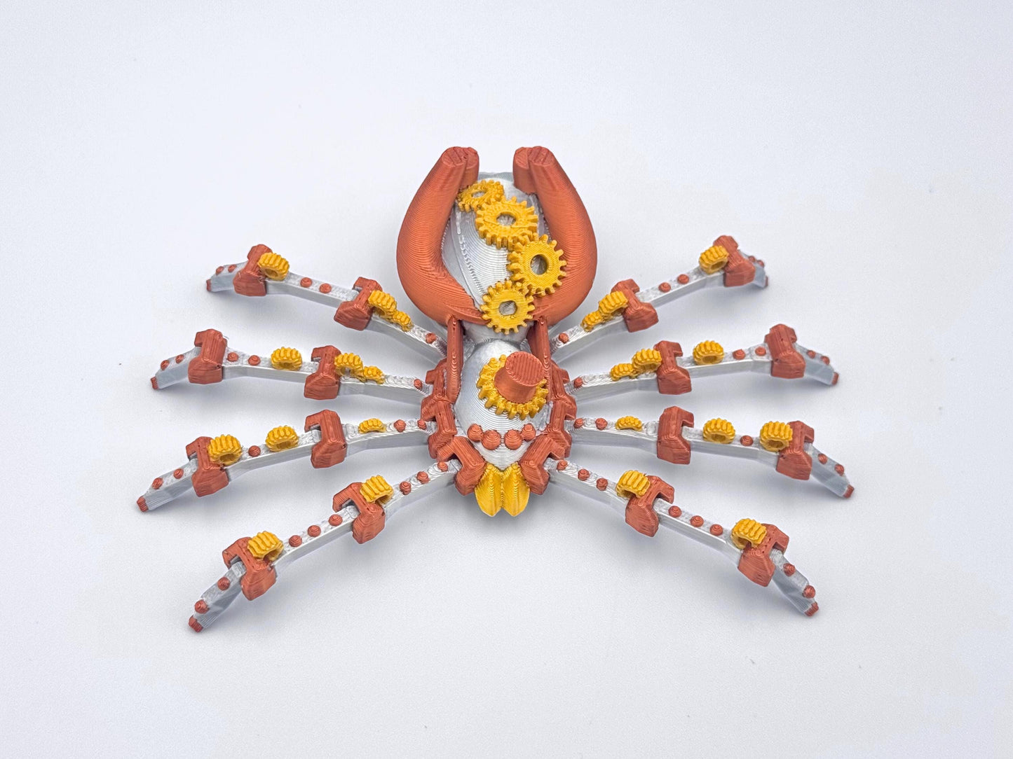 A silver, copper and gold 3D printed steampunk spider fidget with gears in the center of its body and eight legs.