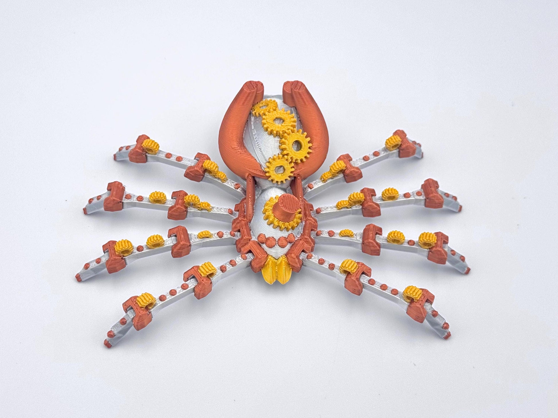 A silver, copper and gold 3D printed steampunk spider fidget with gears in the center of its body and eight legs.