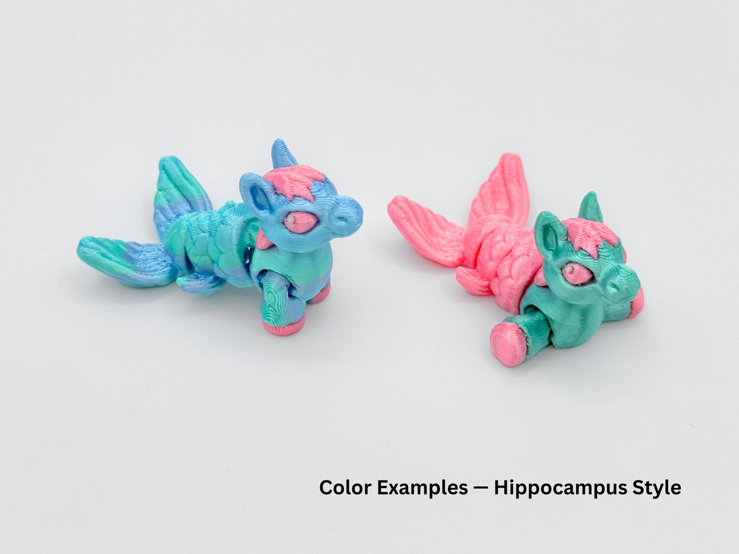Two Hippocampus mini articulated animals with mermaid like tails, shown in bright pastel blends. One is teal and pink, the other rainbow  and pink both posed on a light surface.