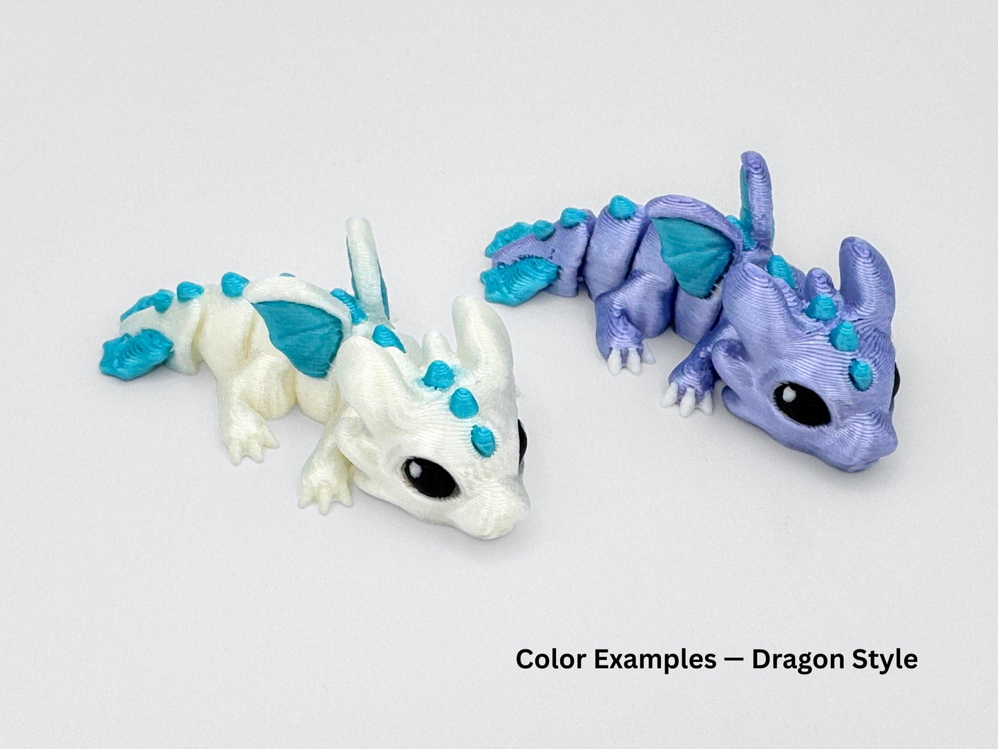 Two Dragon hatchlings mini articulated animals in icy color tones — one white with teal accents and the other lavender with matching teal details. Both feature tiny wings and expressive eyes.