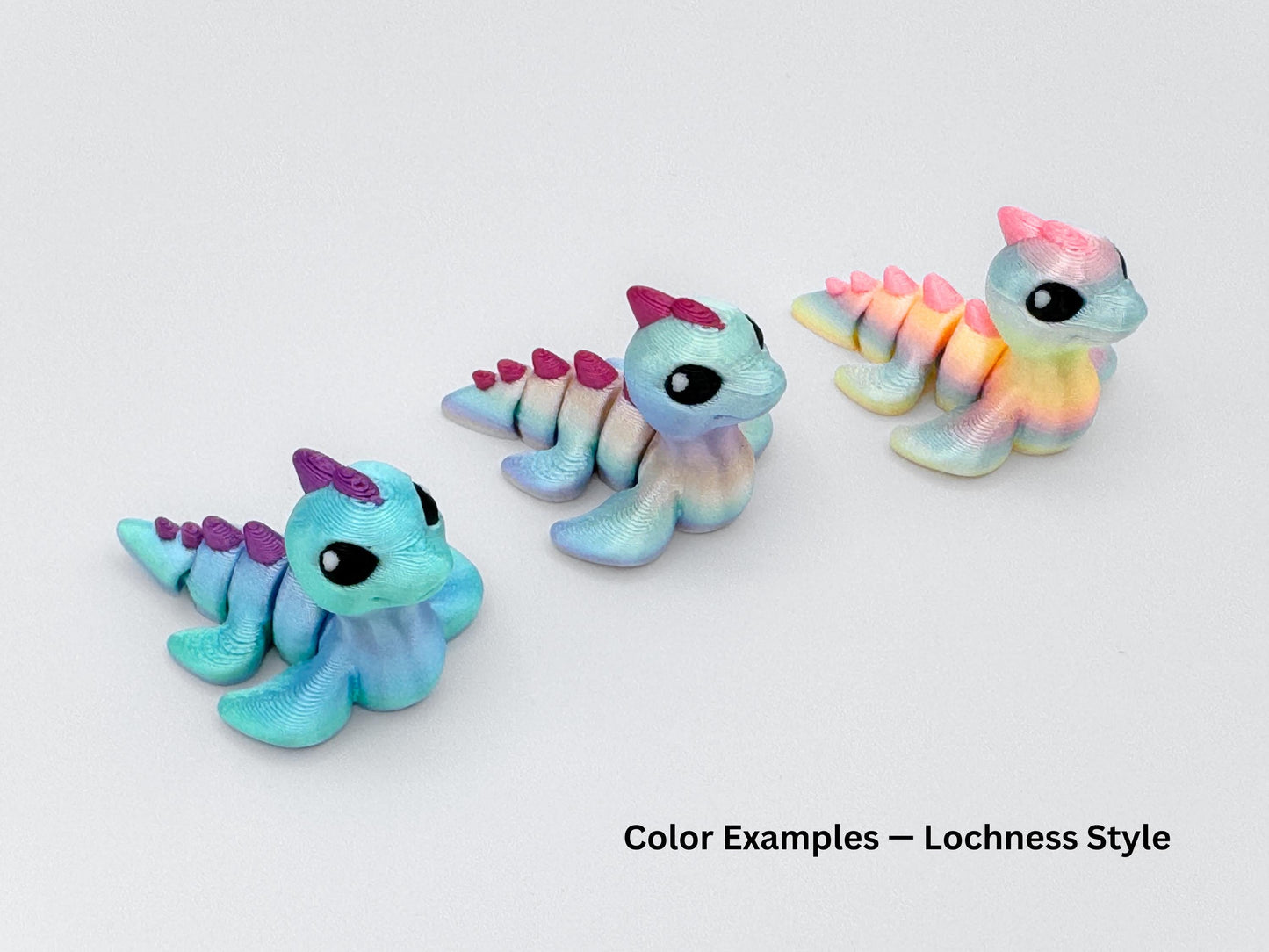 Three Lochness hatchlings in soft pastel colors, featuring rainbow shimmer finishes and gradient spines. Each has large black eyes and small horns, posed on a white background.