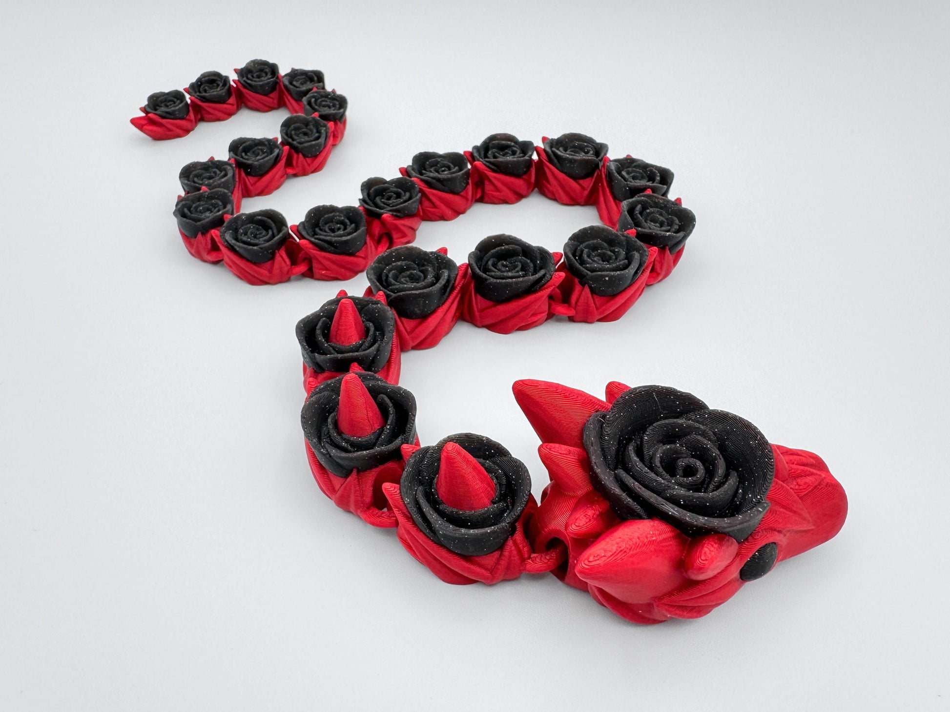 Close-up of a 3D printed articulated rose snake showing a red body with glitter-black rose segments. The camera focuses on texture and connection points between links, capturing sparkle in the black sections and fine surface lines. The tight crop emphasizes sculpted rose forms, flexible joints, and the layered look typical of 3D printed pieces.