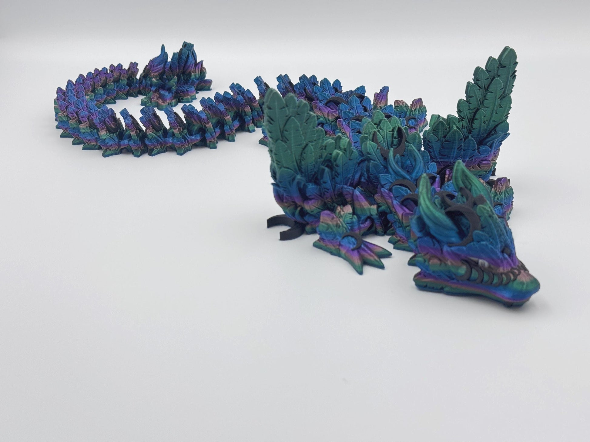 3D printed articulated Lunar Dragon with intricate feathered details, vibrant dark rainbow silk color palette blending shades of blue, green, and purple, and a fully flexible design. Perfect for fantasy collectors, unique decor, or imaginative play.