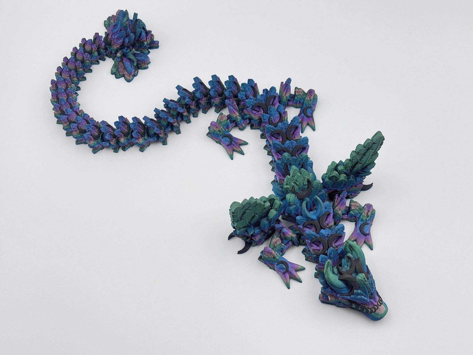 3D printed articulated Lunar Dragon with intricate feathered details, vibrant dark rainbow silk color palette blending shades of blue, green, and purple, and a fully flexible design. Perfect for fantasy collectors, unique decor, or imaginative play.