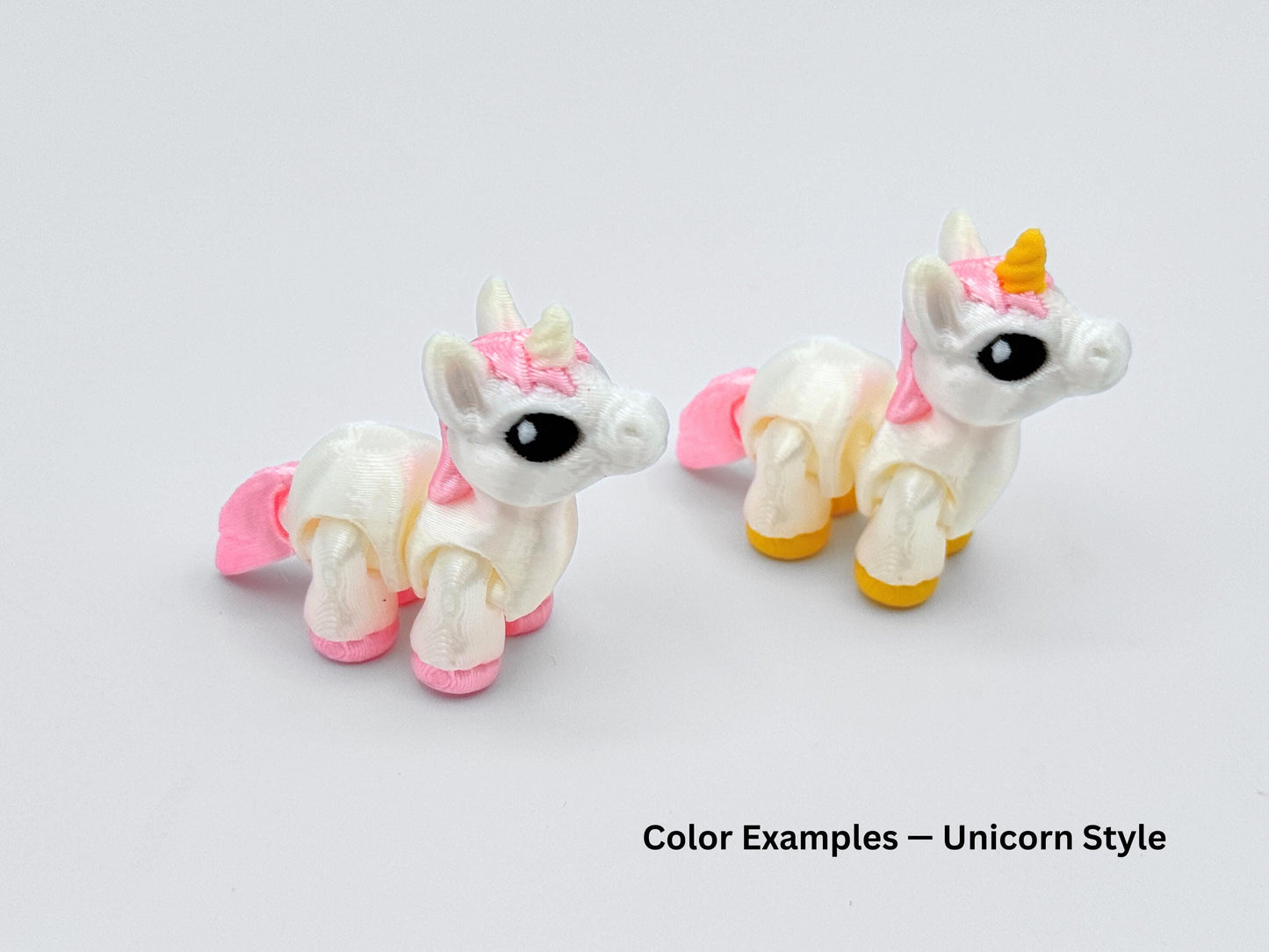 Two Unicorn mini articulated animals with white bodies, pink manes and pastel hooves. One has a golden horn, both feature large black eyes and chubby legs.