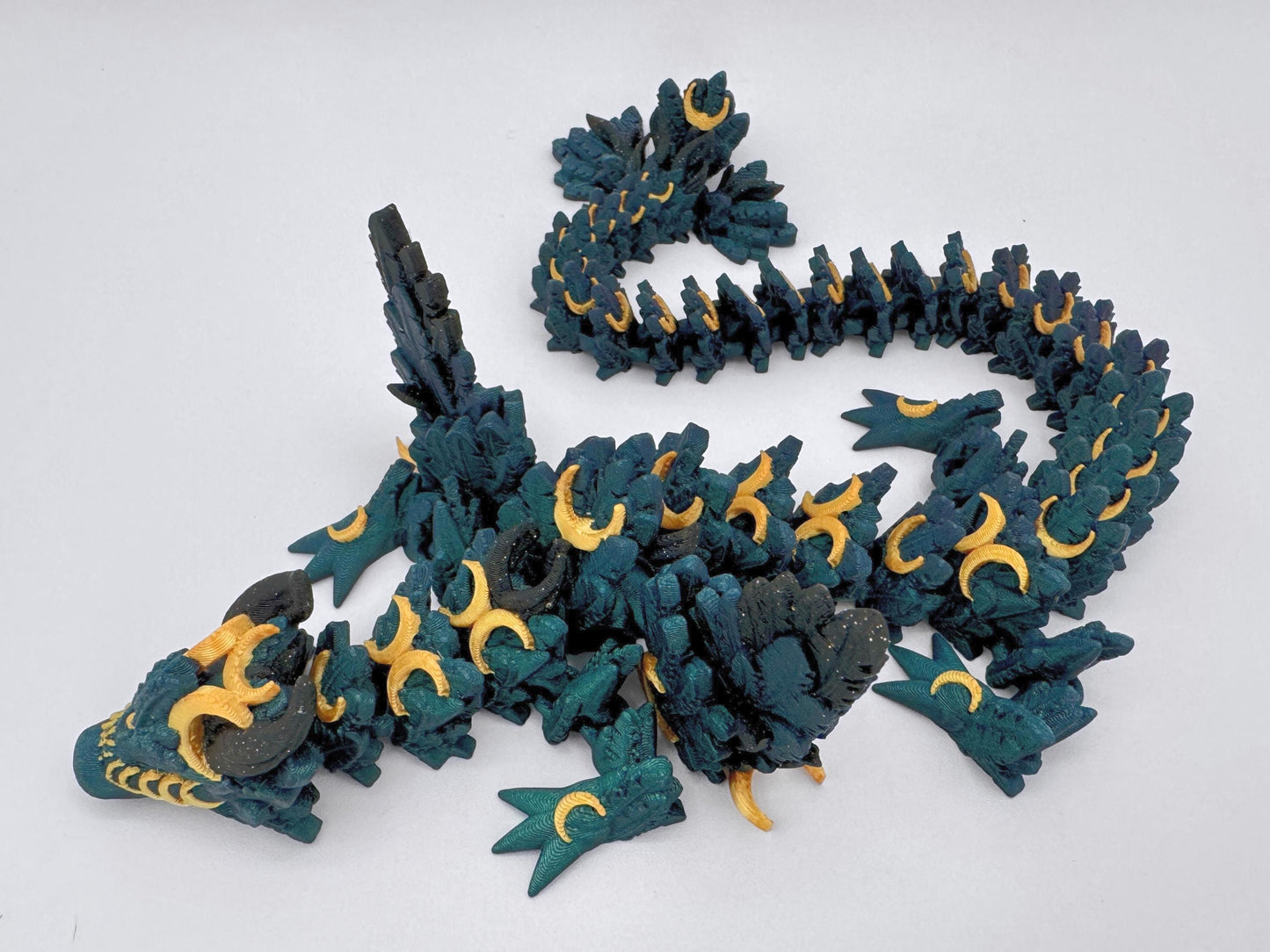 3D-printed articulated Lunar Dragon with intricate feathered details, a chameleon color palette blending deep emerald green with gold crescent moons and shimmering black accents. Features a fully flexible segmented design, making it perfect for fantasy collectors, unique decor, or imaginative play.