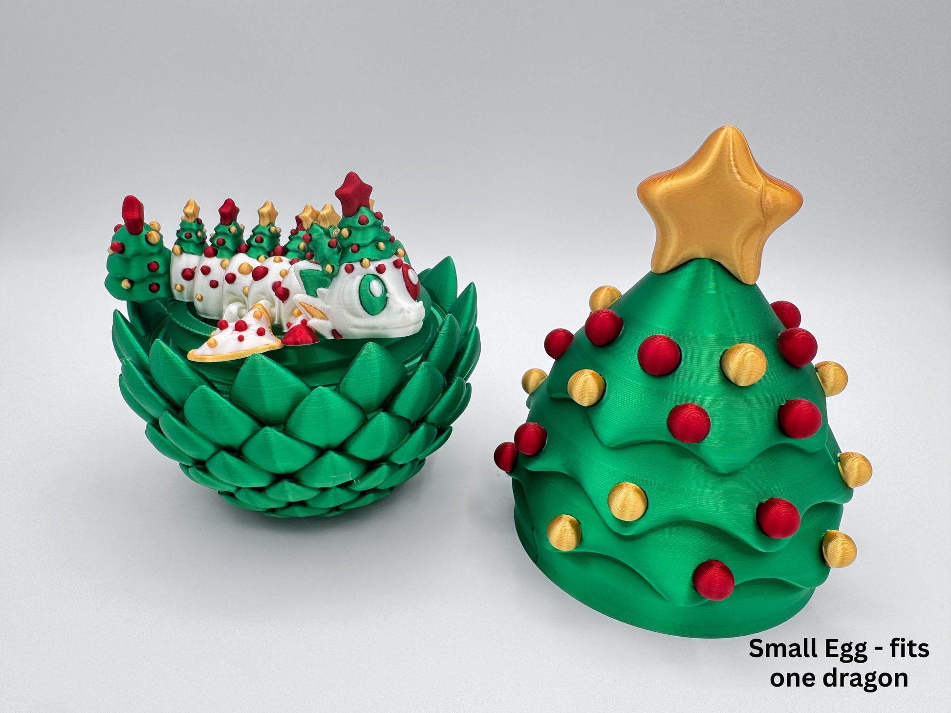 A 3D printed Christmas tree dragon egg shown in two parts: the closed egg on the right with a gold star and red-and-gold ornaments, and the open egg on the left filled with multiple articulated Christmas dragons and tiny tree pieces. Displayed in the green, red, and gold color on a white background as part of the Christmas dragon and egg holiday decor set.