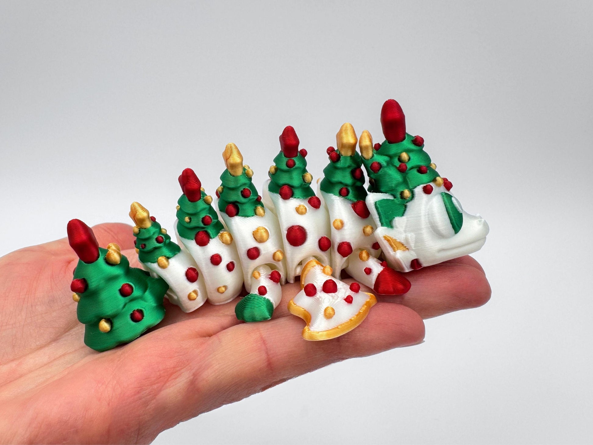 A small 3D printed articulated Christmas tree dragon in green with red ornaments and gold star accents along its body, displayed in a hand to show its size